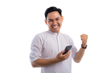 Happy Asian Muslim man holding mobile phone, gesturing yes with clenched fist, getting good news isolated on transparent background