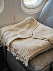 Everyday objects - for downstream advertisement and design: A soft, beige blanket rests on an airplane seat, showcasing a view of clouds through the window.