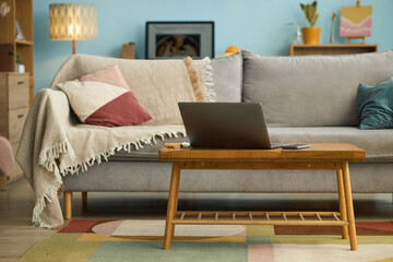 Cozy modern living room featuring gray sofa with colorful cushions, wooden coffee table with laptop, and warm lighting creating inviting atmosphere