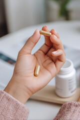 hand holding yellow capsule near open medicine bottle symbolizing oral health and wellness. soft lighting adds calm and healthy vibe