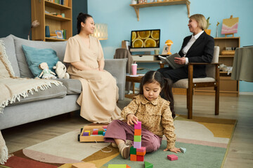 Caregiver engaging with child stacking blocks in a cozy living area, woman and child creating an...