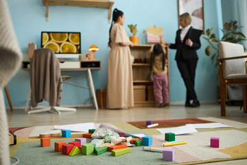 Scene displaying family engagement in homely setting with colorful toy blocks scattered on floor emphasizing togetherness and interaction among people present