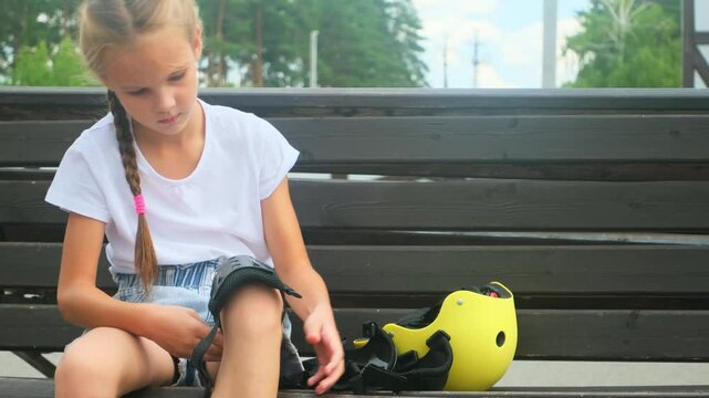 Young skater girl putting on protective shin guards and knee pads for skating. child rollerblader preparing for a ride in skatepark in summer