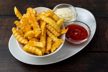 Crinkle-cut fries with ketchup and mayonnaise on a white plate.