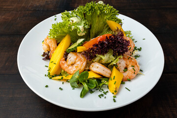 Grilled shrimp with mango, salad greens, and balsamic glaze on white plate.