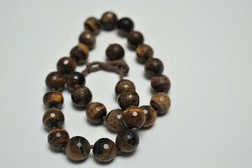 The jewelry is a bracelet or necklace made of round stones of tiger eye isolated on white