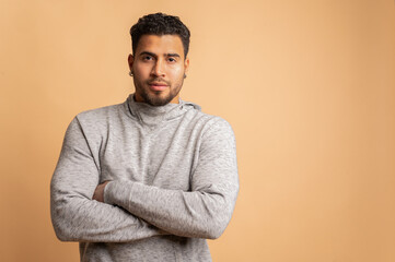 Colombian man posing with crossed arms in studio on beige background