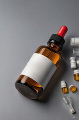 Brown glass bottle with blank label and various small vials placed on a gray surface
