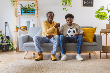 Cheerful grandfather and grandson watching soccer match together at home