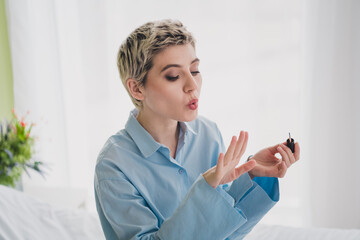 Charming young woman painting nails with blue shirt and short hair, enjoying a relaxed morning at...