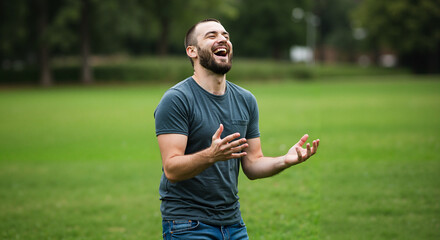 Joyful man laughing while standing in a green park  