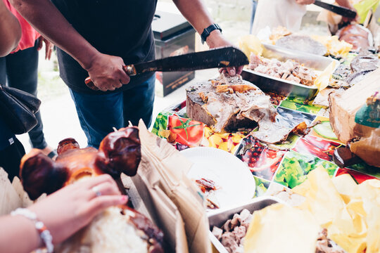 Man's hand slicing on wooden chopping board of the popular, delicious and crispy roasted pig known as "lechon baboy" (in the Philippines, Spain, Cuba, etc.). Selective focus. Copy space.