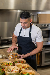 A chef in a black apron packs fresh, healthy takeout meals in eco-friendly bowls. A...