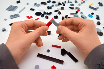 Child's hands assembling colorful plastic construction bricks on a white table. Educational and creative activity to support development.