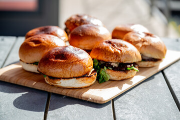 Vue sur plusieurs hamburgers faits maison avec des steaks, de la salade, du fromage fondant, le tout disposé sur une planche en bois.