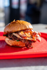 Hamburgers faits maison au fromage fondant et au bacon, disposés sur un plateau rouge.