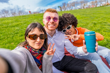 Group of happy multi ethnic friends taking a selfie in the park showing victory sign and reusable coffee cup