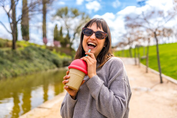 Fototapeta premium Happy woman drinking refreshing beverage in a park by the river