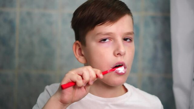 A ten year old boy is concentrating on brushing his teeth with a red toothbrush