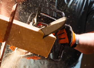 Worker uses a chainsaw to cut a plank into two pieces while working