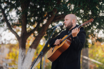 Musician playing acoustic guitar and singing into microphone in park