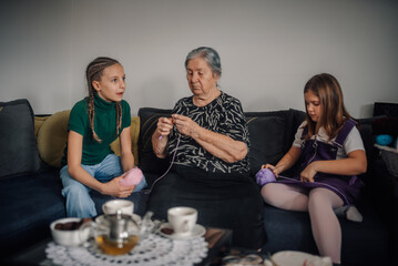 Grandmother teaching granddaughters knitting on sofa in living room