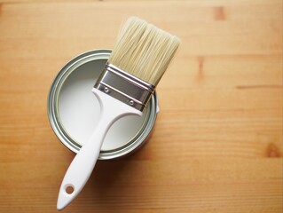 White paint can with brush resting on wooden tabletop