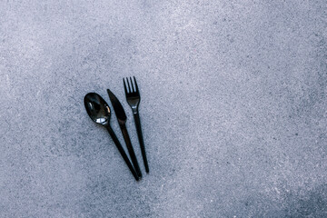 Black plastic spoon, knife, and fork on a gray stone background with empty space for text or design