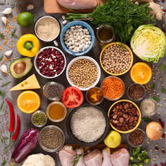 Large set of balanced nutrition products on gray concrete background, top view. Vegetables, fruits, nuts, grains, olive oil, green herbs.