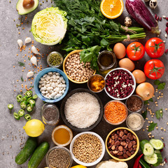 Large set of balanced nutrition products on gray concrete background, top view. Vegetables, fruits, nuts, grains, olive oil, green herbs.