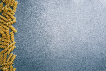 Top view of uncooked fusilli pasta arranged along the left edge on a textured gray surface with...