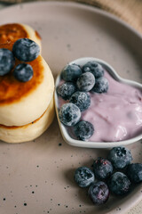 Delicious cottage cheese pancakes served with creamy berry yogurt and fresh blueberries in a heart-shaped bowl on a ceramic plate