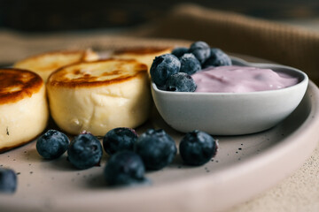 Delicious cottage cheese pancakes served with creamy berry yogurt and fresh blueberries in a heart-shaped bowl on a ceramic plate