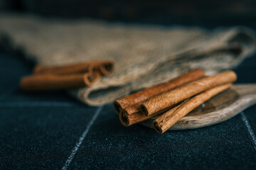 Cinnamon sticks arranged on a wooden plate and burlap fabric, with rustic black tile background