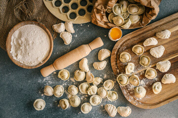 Flat lay of homemade dumplings and pelmeni with flour, rolling pin, cutting board, and egg yolk on...