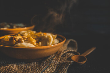 Traditional dumplings served in a rustic clay bowl with fried onions and steam rising, placed on burlap fabric in warm, moody lighting