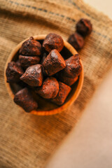 Rustic wooden bowl filled with rich cocoa-dusted chocolate truffles on burlap fabric with a dark moody background