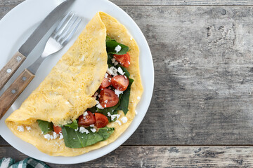 Stuffed omelette with tomatoes and spinach on wooden table. Top view. Copy space