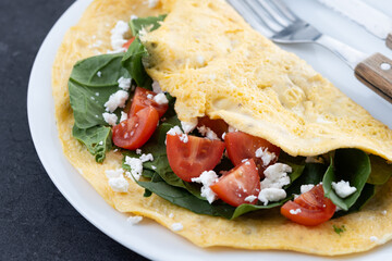 Stuffed omelette with tomatoes and spinach on black stone