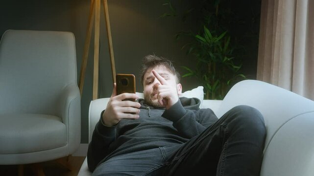 Frustrated young man exhausted from watching short videos on phone, feeling wasted time