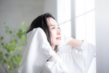 Profile of a smiling woman towel drying wet hair in the morning or after a bath on a backlit window sill.