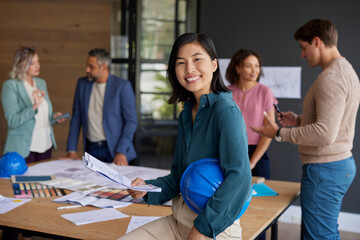 Smiling architect holding blue helmet and new project
