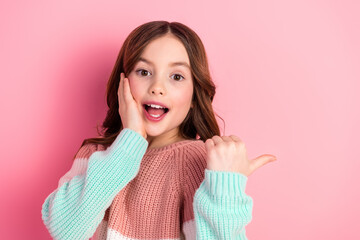Adorable young girl in stylish casual sweater posing against pink background showcasing happiness...