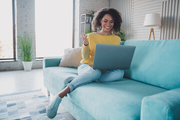 Fototapeta premium Young woman relaxing on a couch while using a laptop in a cozy and modern interior