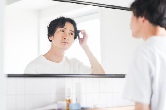 鏡を見ながら髪を触る若いアジア人男性。メンズビューティー