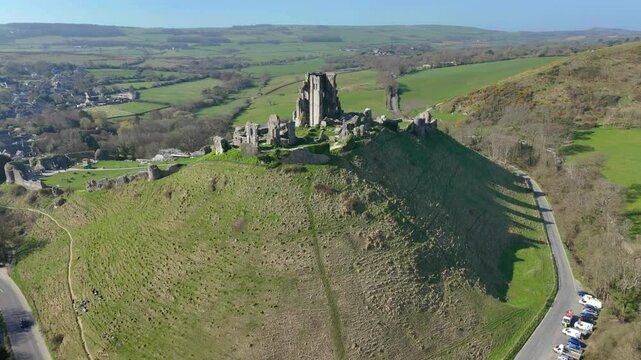 drone view of the dramatic ruins of Corfe Castle stands on a natural hill overlooking the village