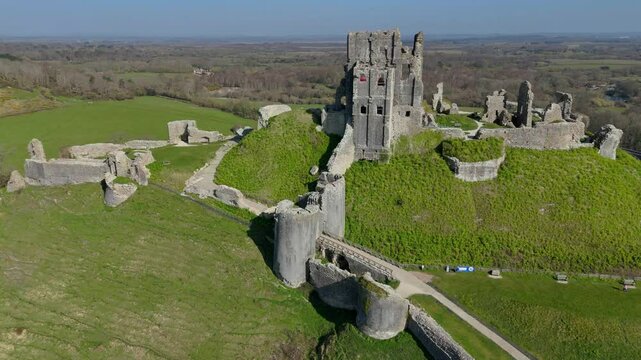 The ruins of Corfe Castle on a green hill in the Purbeck Hills, England on a sunny day with blue sky