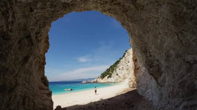 Male tourist walks on the Platia Ammos beach in Ithaca island, Greece. Static shot from inside the cave