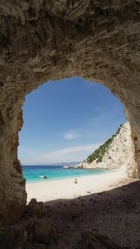 Male tourist sits on the Platia Ammos beach in Ithaca island and enjoys the beauty of the landscape. Static shot from inside the cave. Vertical