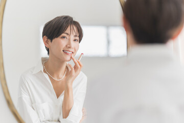 鏡を見ながら口紅を塗る女性。/メイクアップ